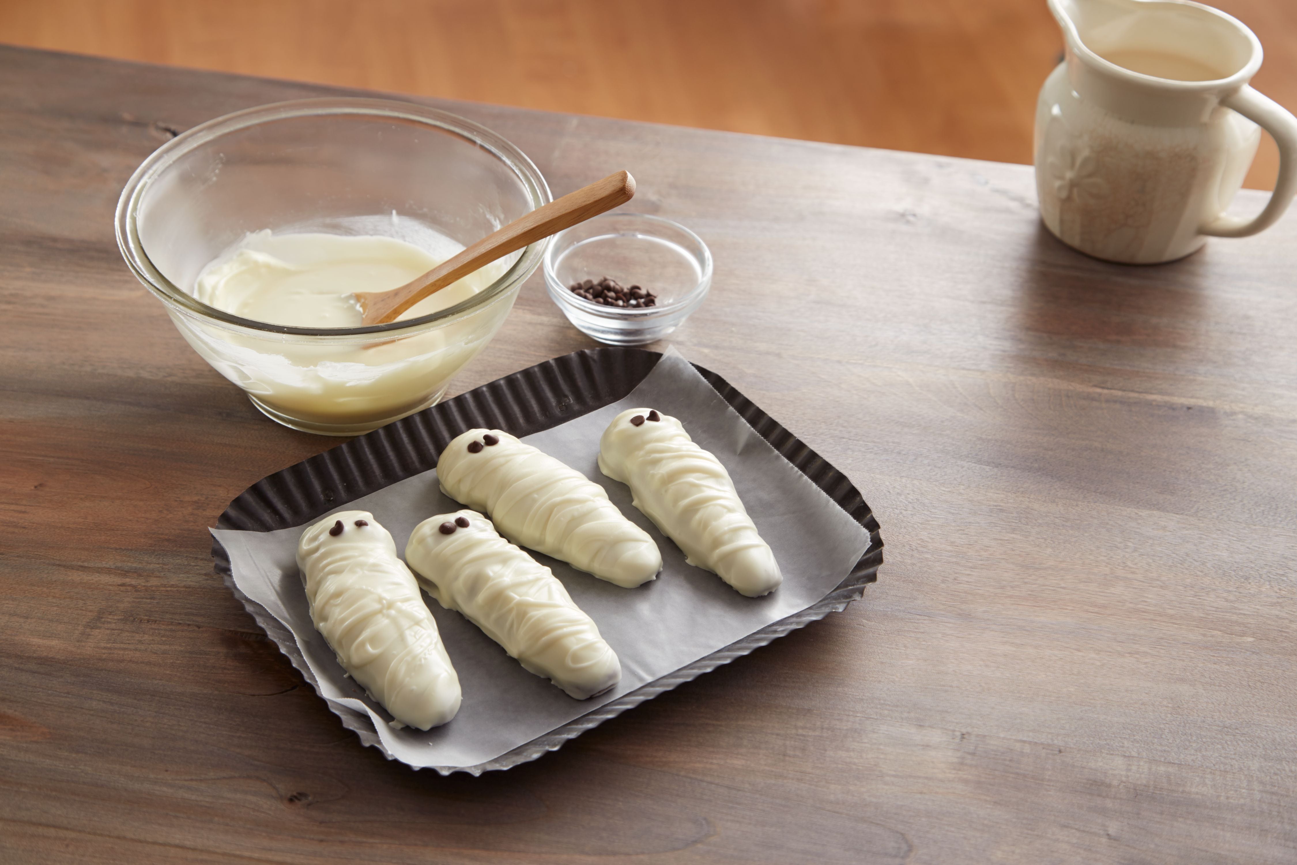 Quatro biscoitos de múmia branca em uma forma, pronta para assar.